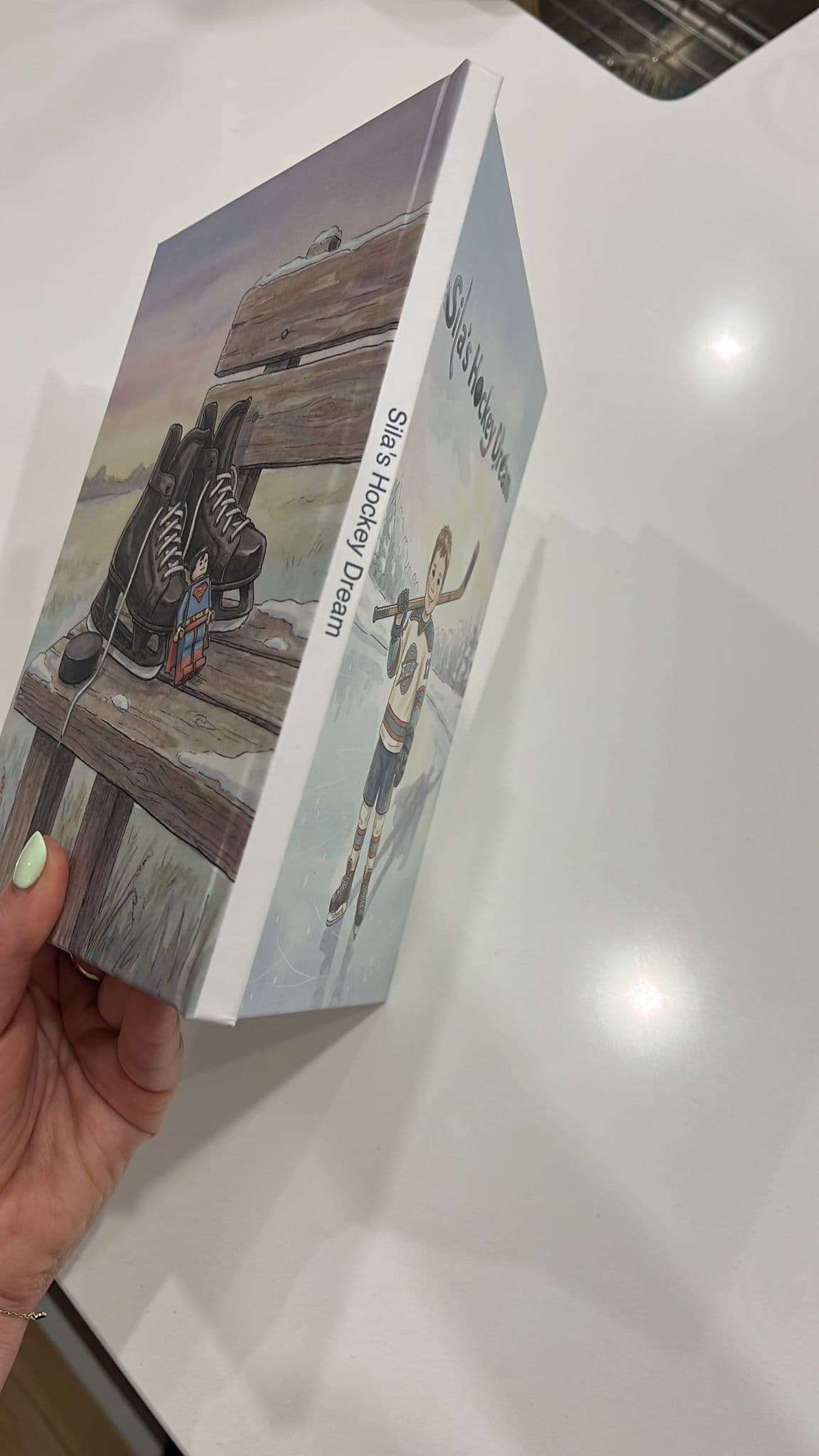A hand holding Sila’s Hockey Dream at an angle, showing its printed spine, hardcover boards and back-cover artwork