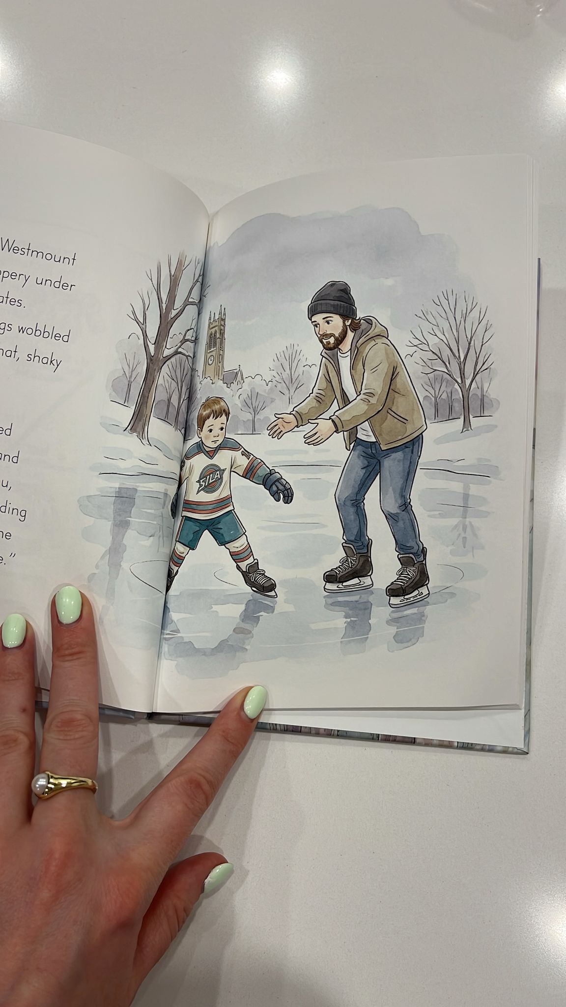 Product photograph: a hand holding Sila’s open book with an illustrated skating scene